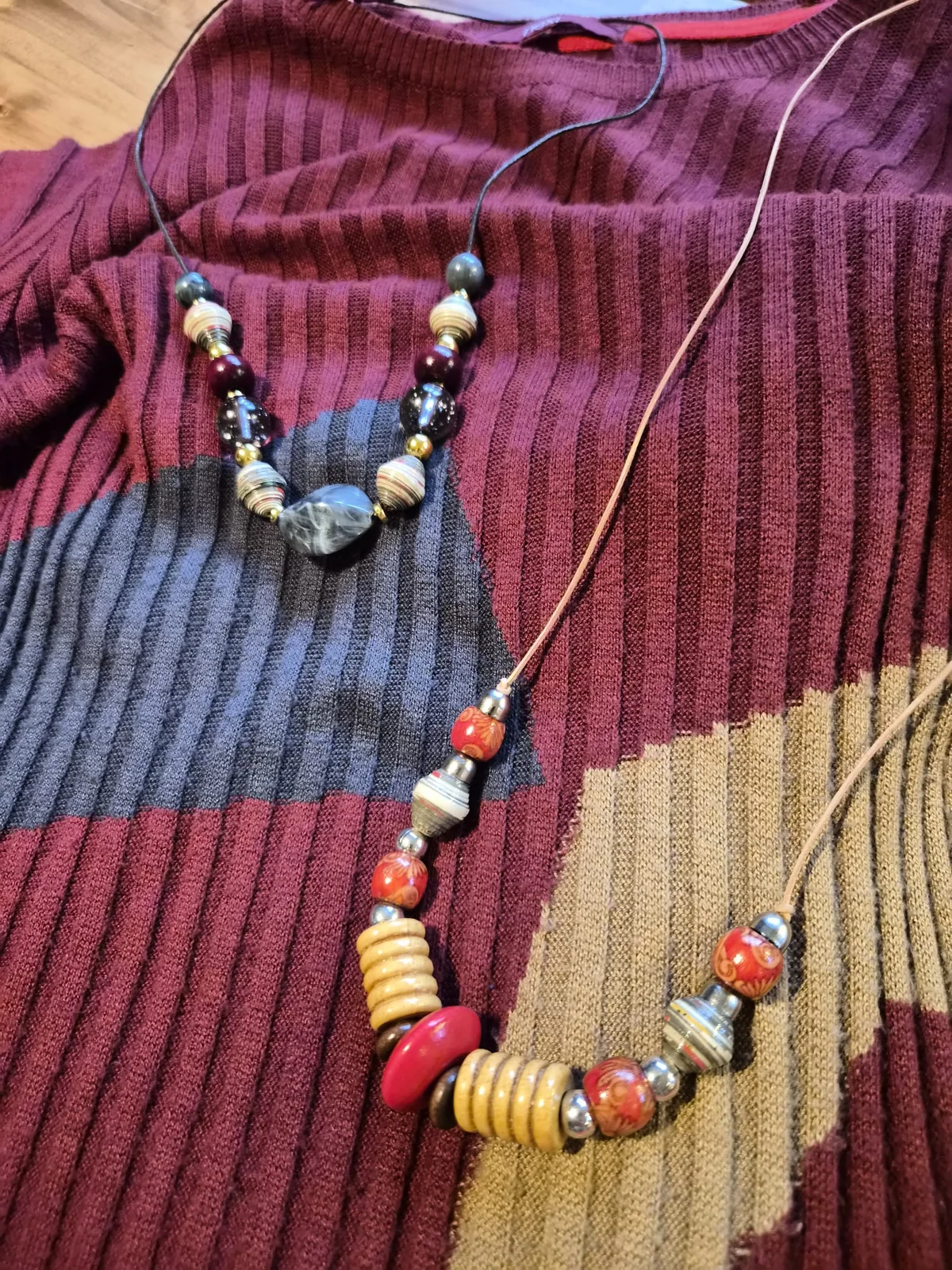 Two different handmade necklace interpretations arranged on the same wine-coloured dress